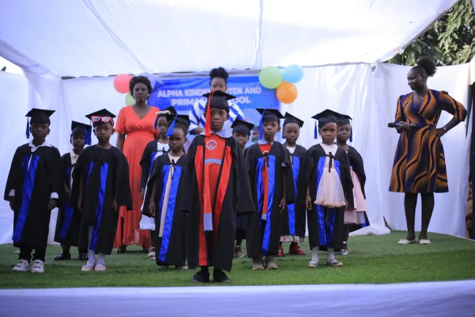 Children wearing graduation gowns on a school stage.